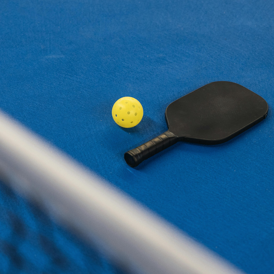 Pickleball paddle and ball resting on court.