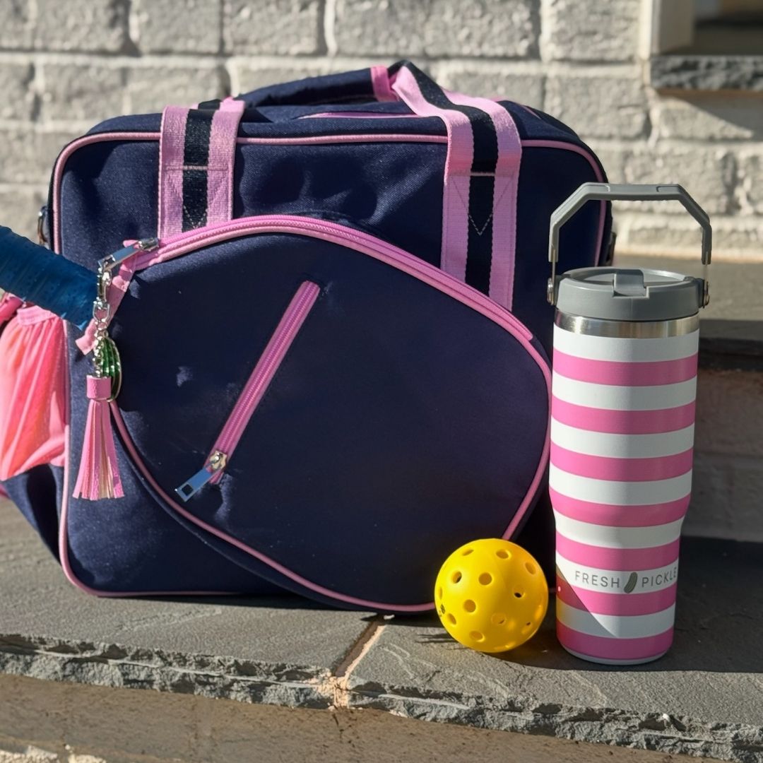 Pink and navy pickleball bag, striped tumbler, yellow pickleball, and paddle on outdoor step