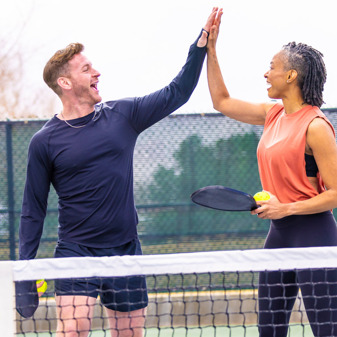 Smiling couple high-fiving on pickleball court with paddles and ball