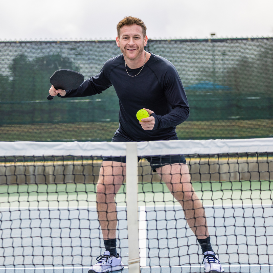 Man playing pickleball on outdoor court, holding paddle and ball, wearing athletic gear