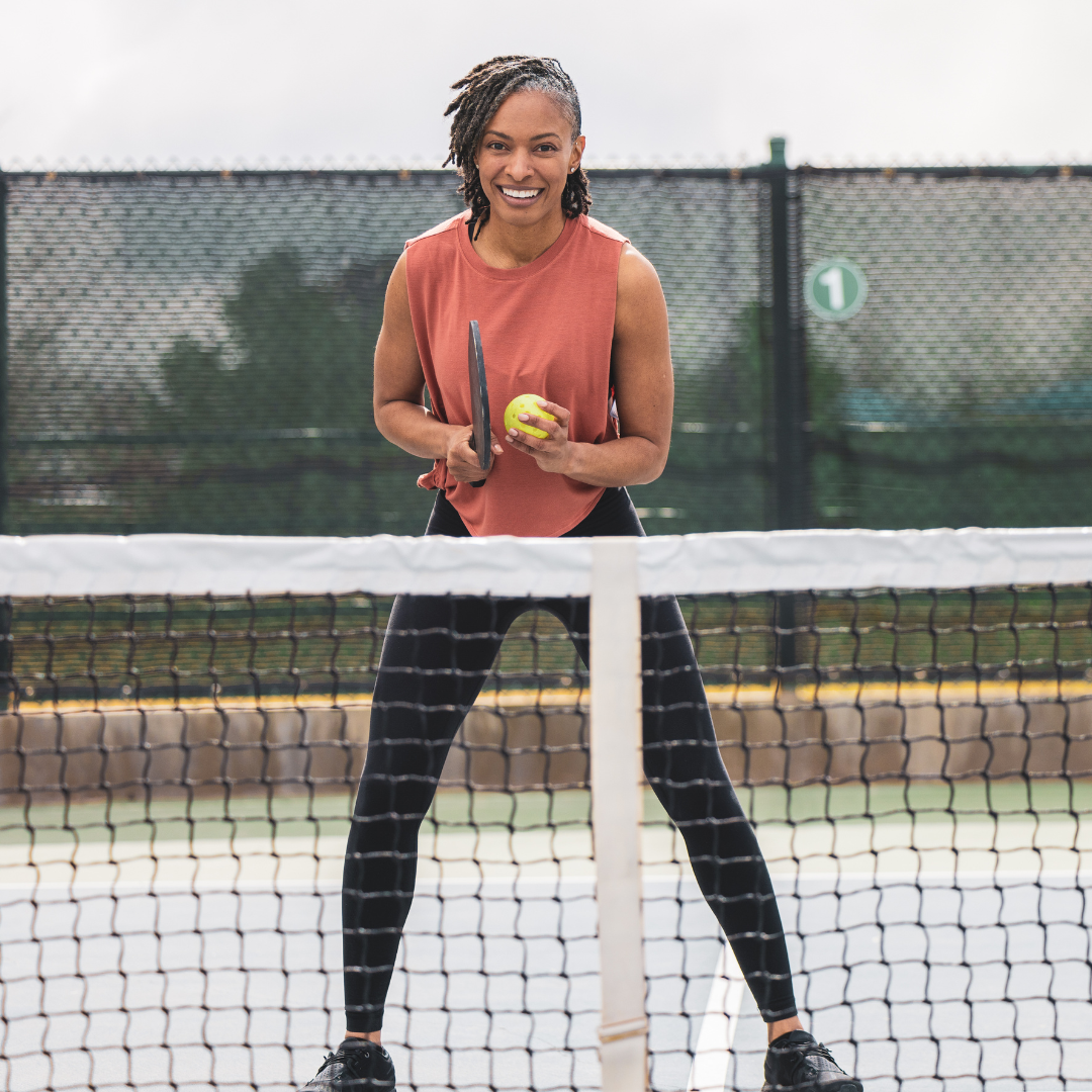 Woman holding pickleball paddle and ball on outdoor pickleball court, ready to play