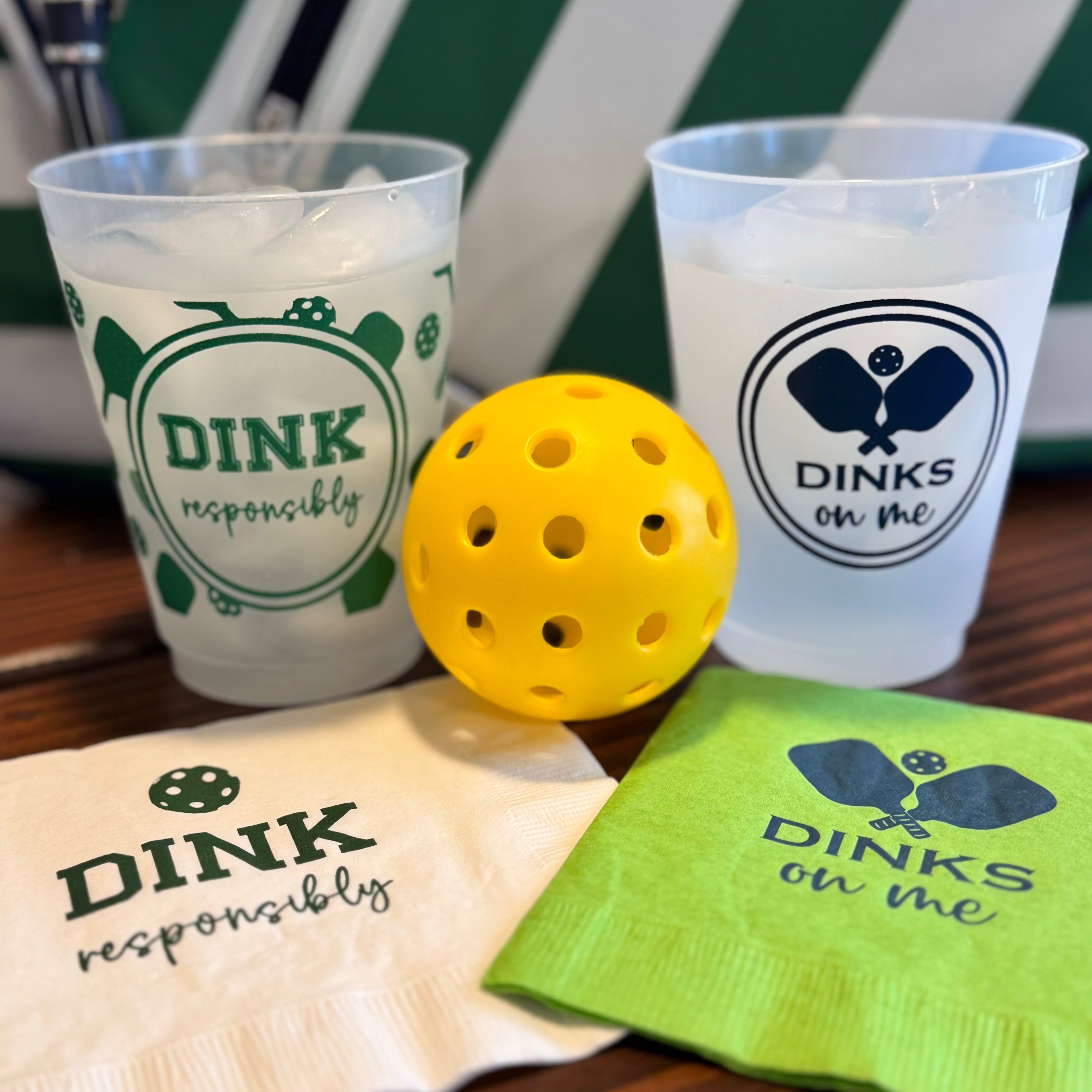 Pickleball-themed cups, napkins, and a yellow pickleball on a wooden table