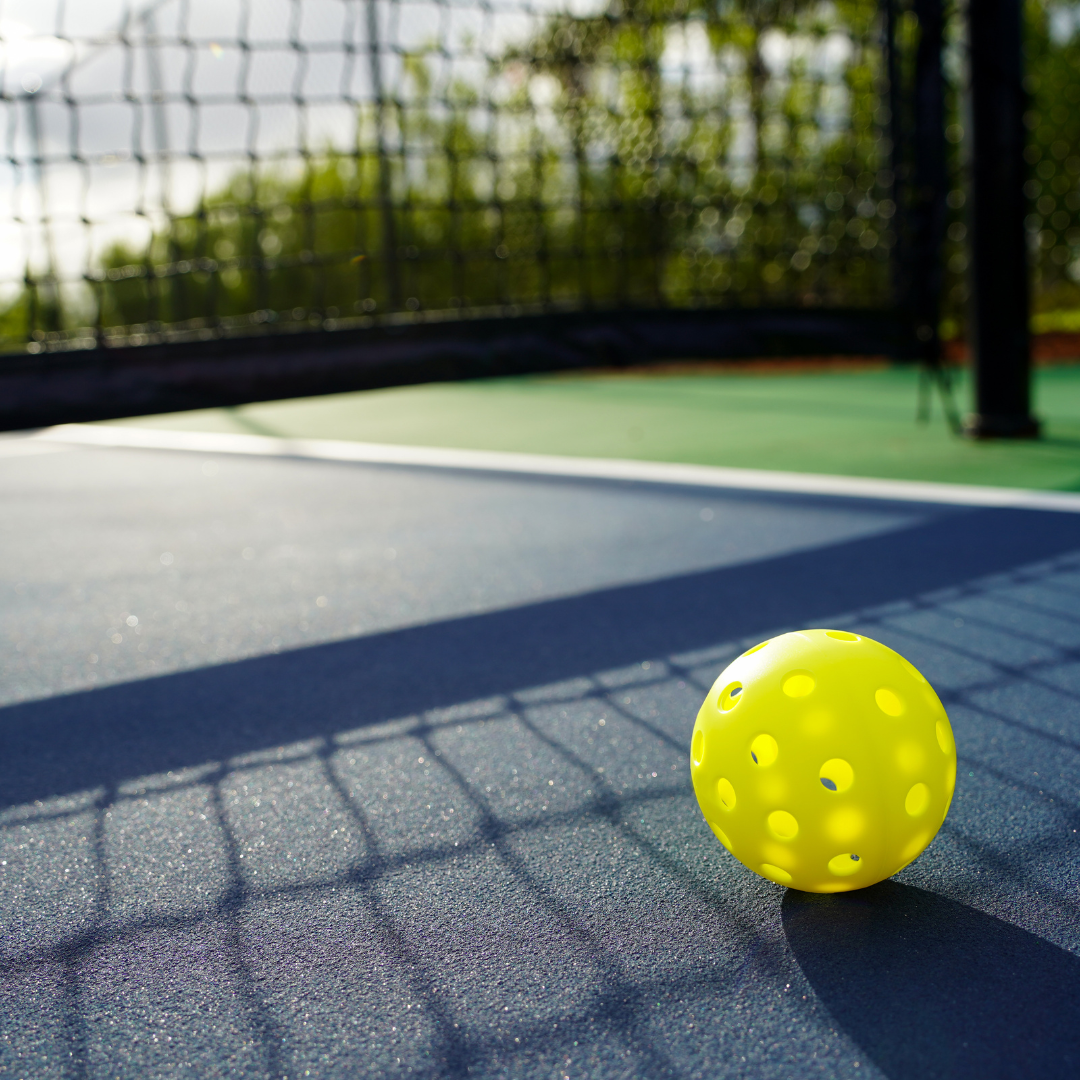 Yellow pickleball on outdoor pickleball court near net in sunlight
