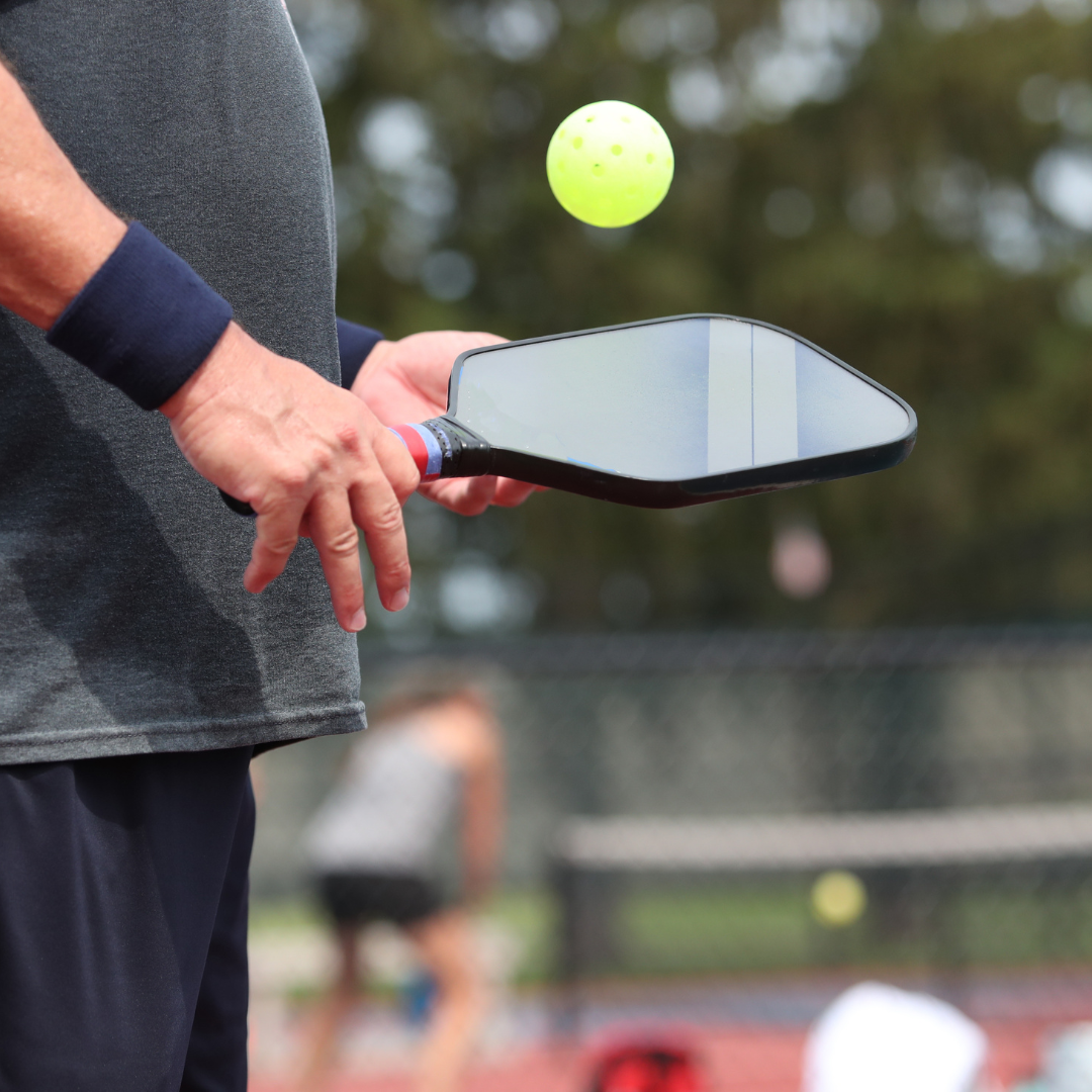 Pickleball player holding paddle and yellow perforated ball on outdoor court