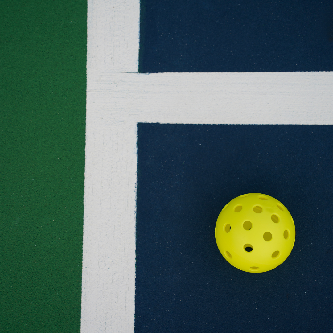 Yellow pickleball on blue and green court with white lines