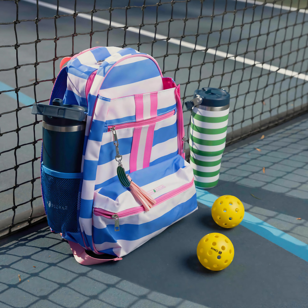 Striped pickleball bag with water bottles and yellow pickleballs on court by net