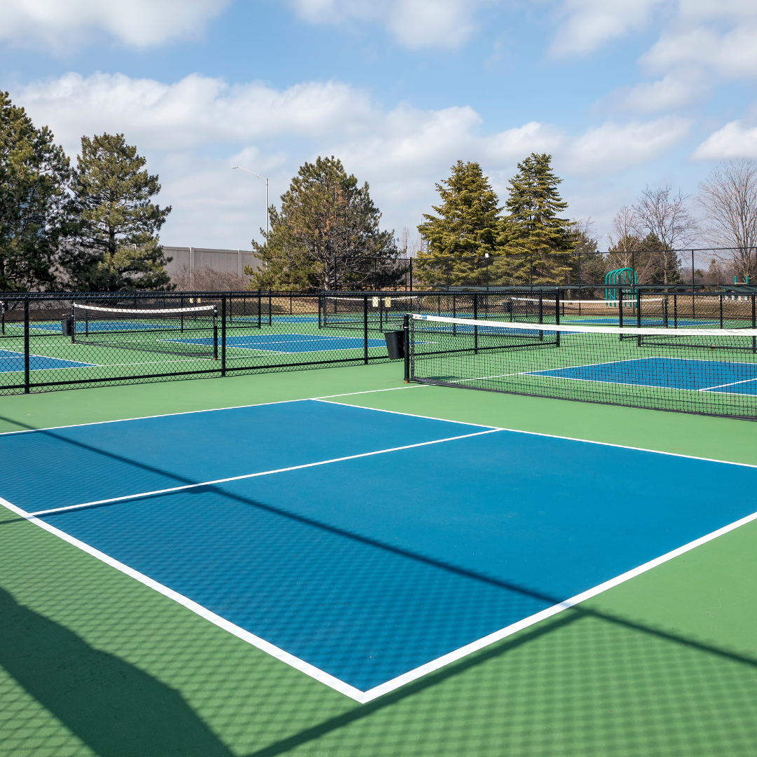 Outdoor pickleball courts with blue and green surfaces under a partly cloudy sky