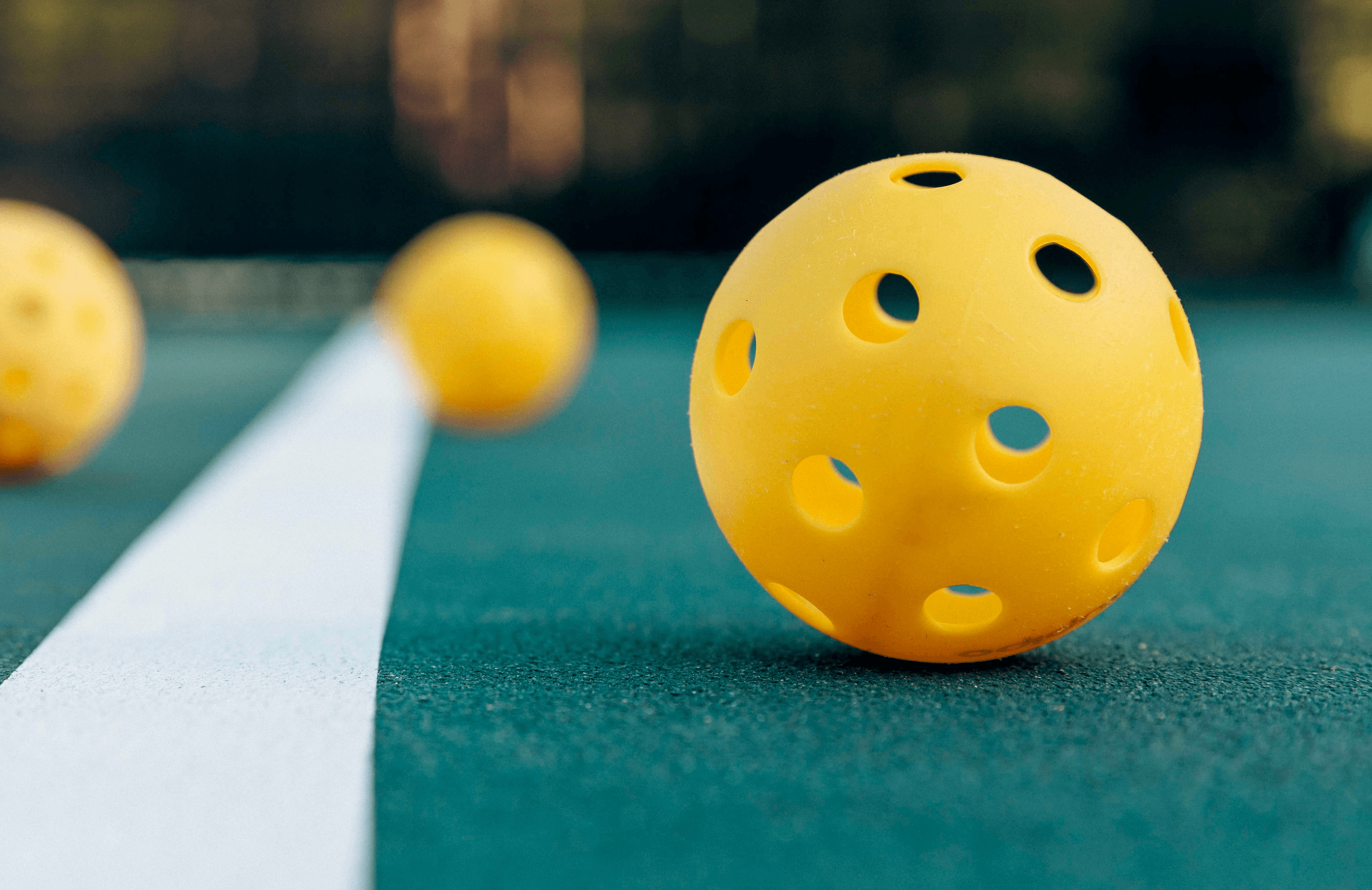 Close-up of yellow pickleball balls on an outdoor court with a white line.