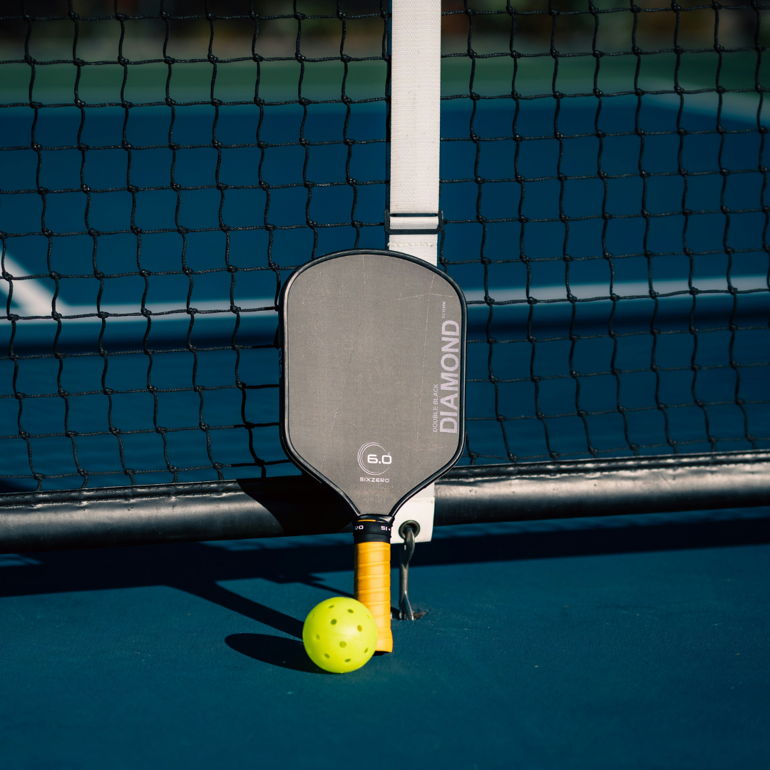 Pickleball paddle with yellow grip and pickleball on court near net