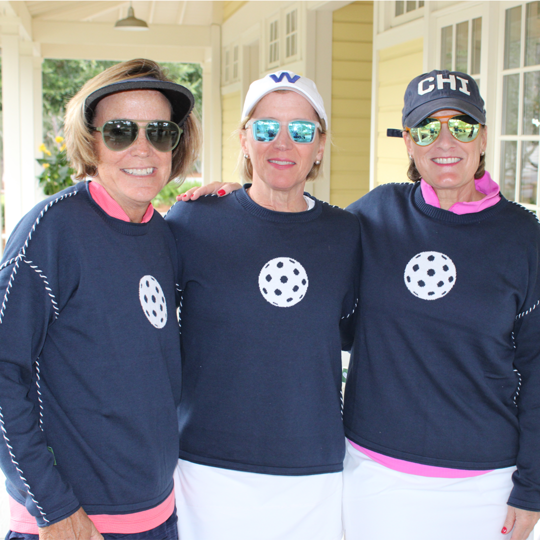 Three women in navy pickleball sweaters and sunglasses posing outdoors
