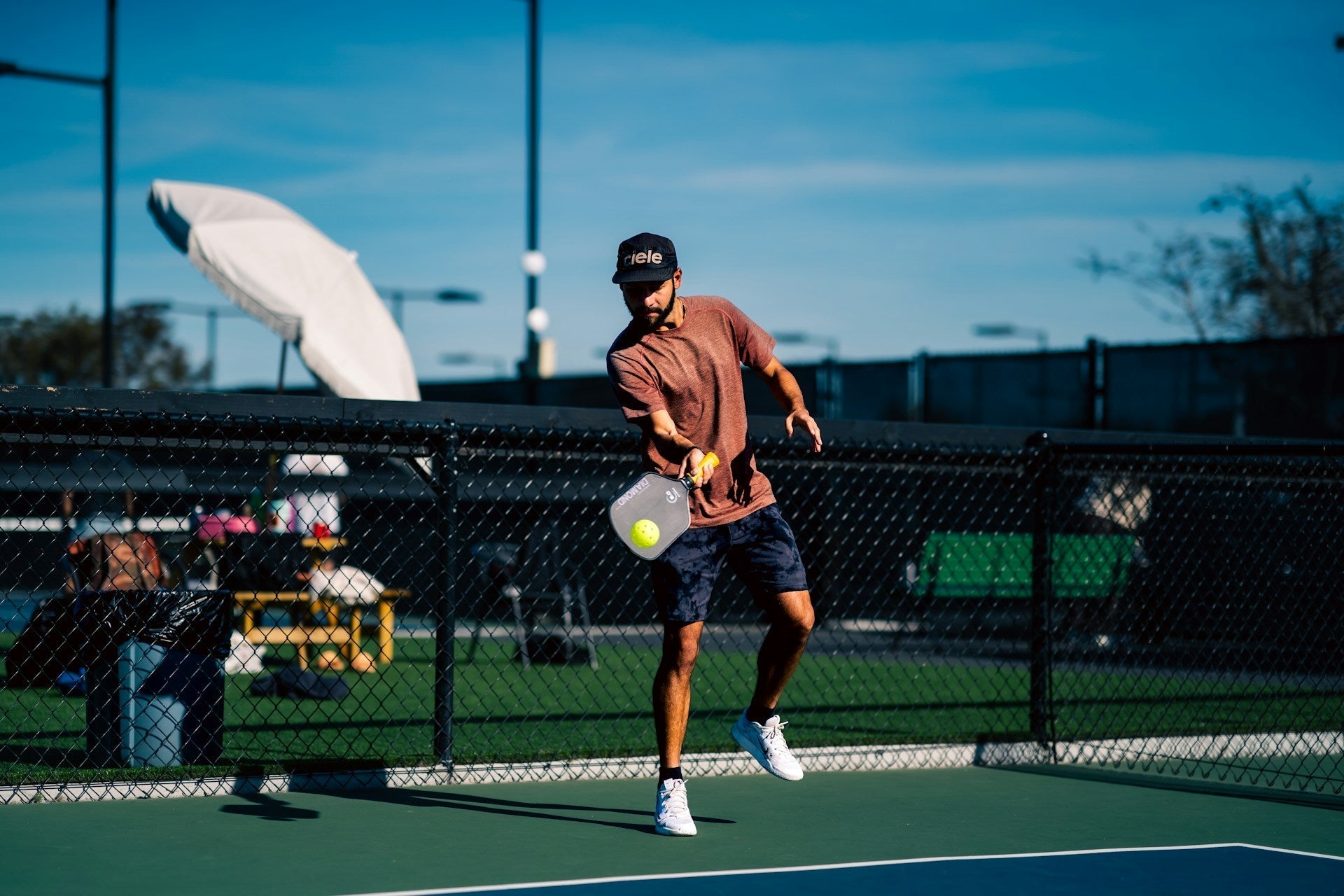 Man playing pickleball outdoors in athletic gear, swinging paddle at yellow pickleball