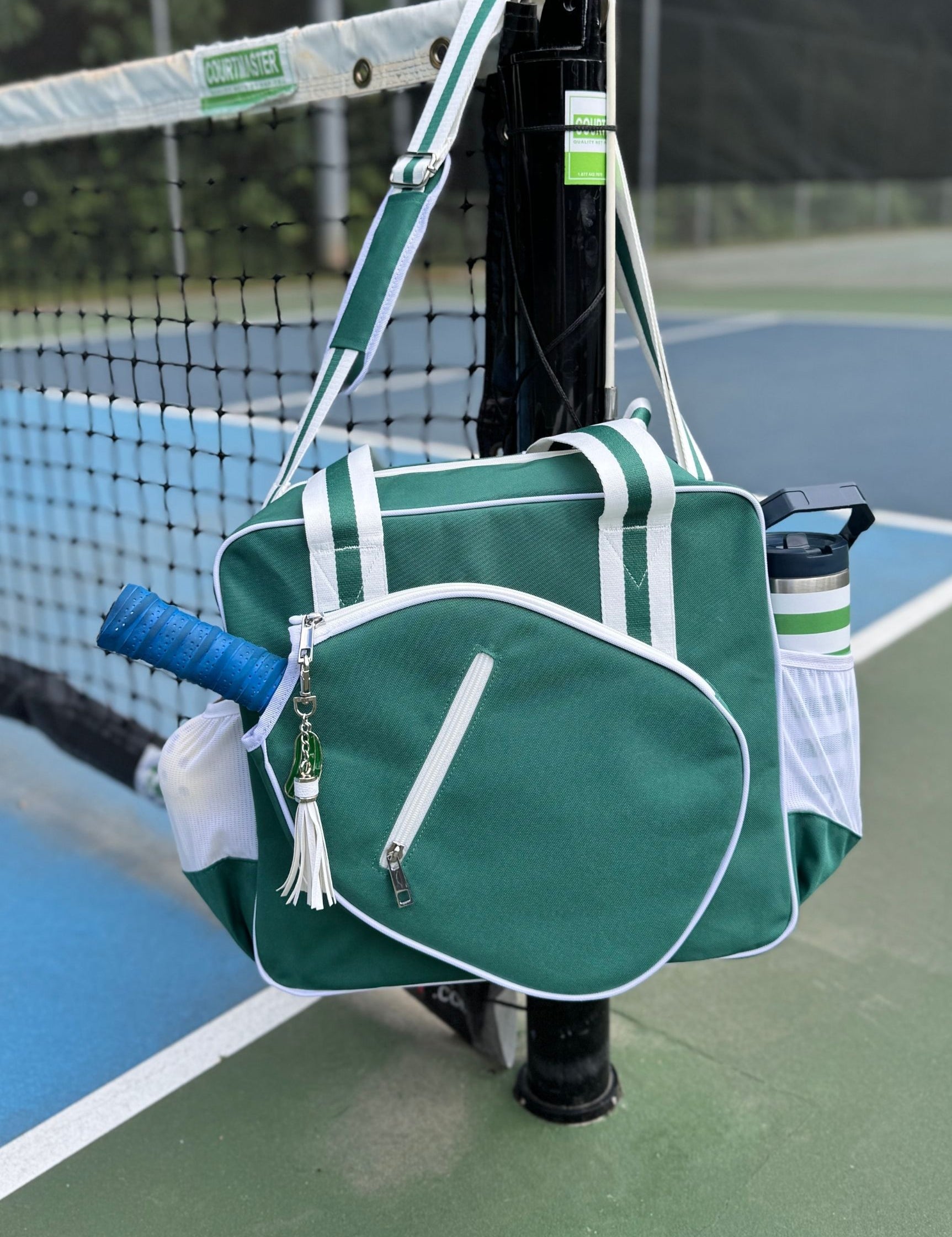 Green pickleball bag with blue paddle and water bottle on outdoor pickleball court