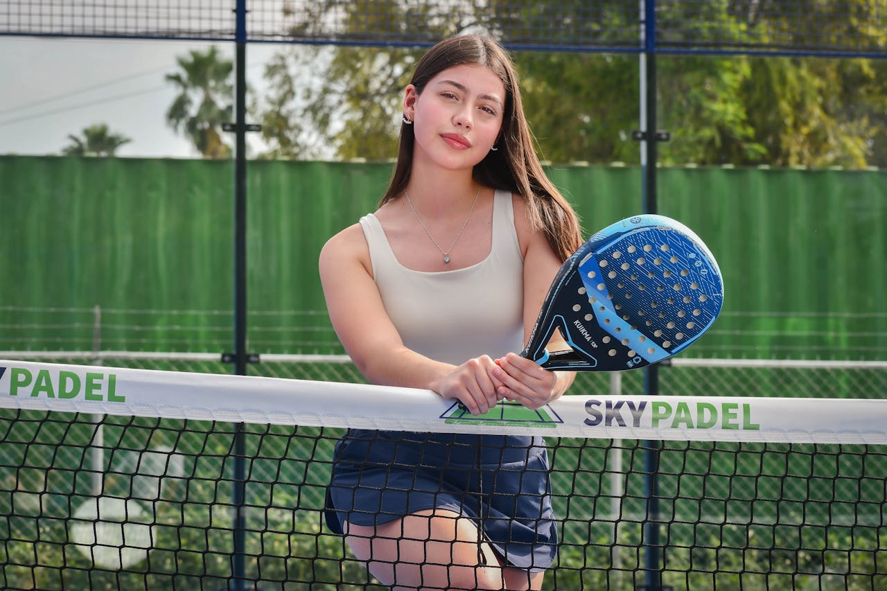 Woman in athletic outfit holding blue pickleball paddle on outdoor court