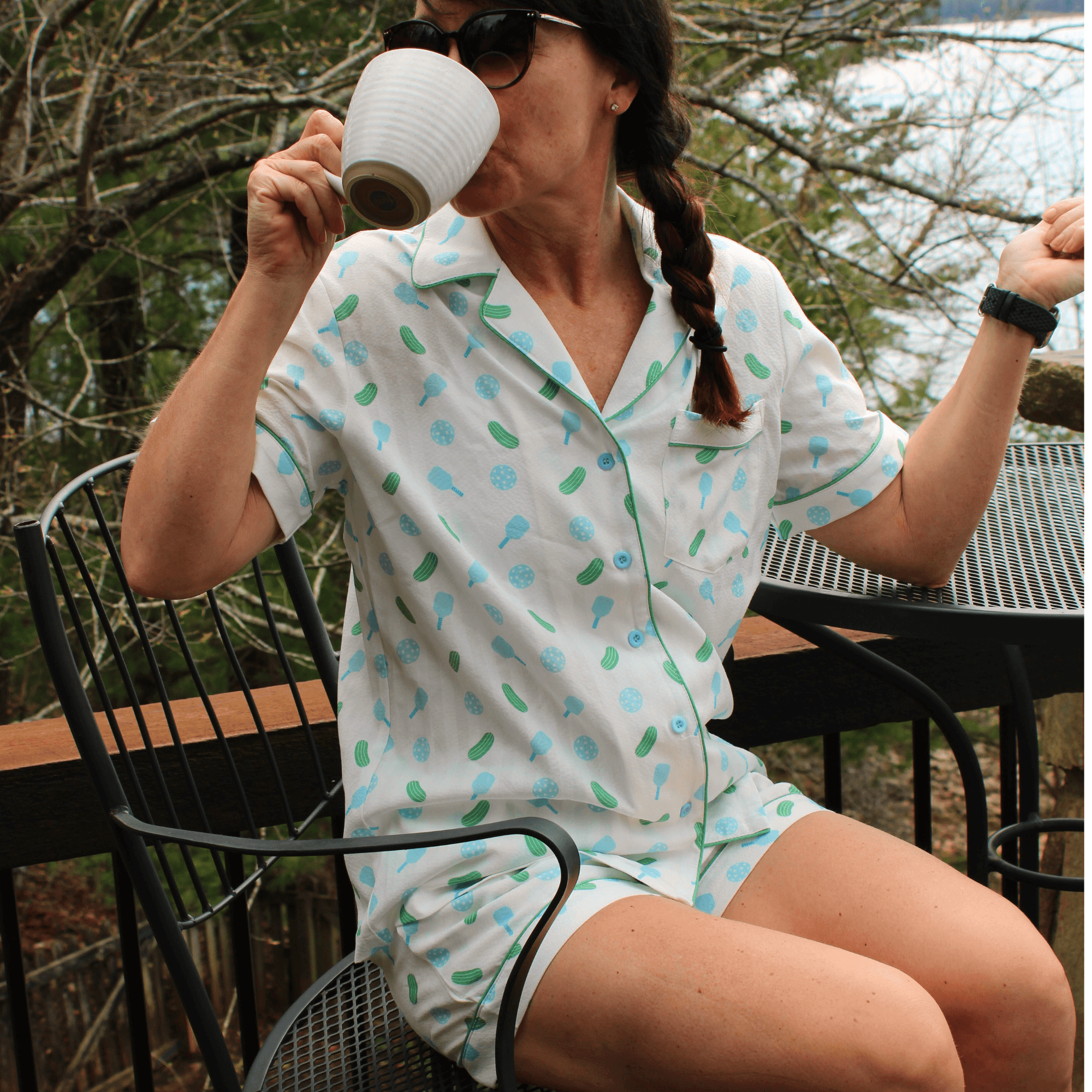 Woman in pickleball print short-sleeve pajamas drinking coffee outdoors on patio