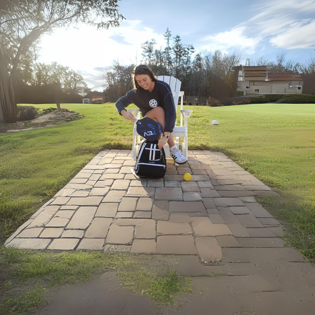 Woman in casual sportswear sitting outdoors, packing a pickleball paddle in a sporty bag on patio.