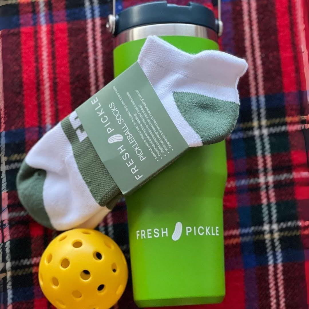Green pickleball tumbler, white athletic socks, and yellow pickleball on plaid blanket