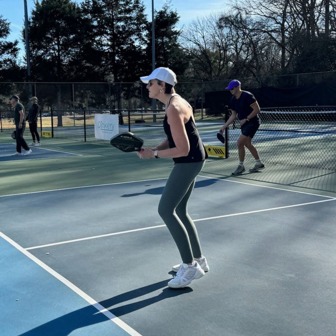 Woman in athletic apparel playing pickleball on an outdoor court under sunny weather.