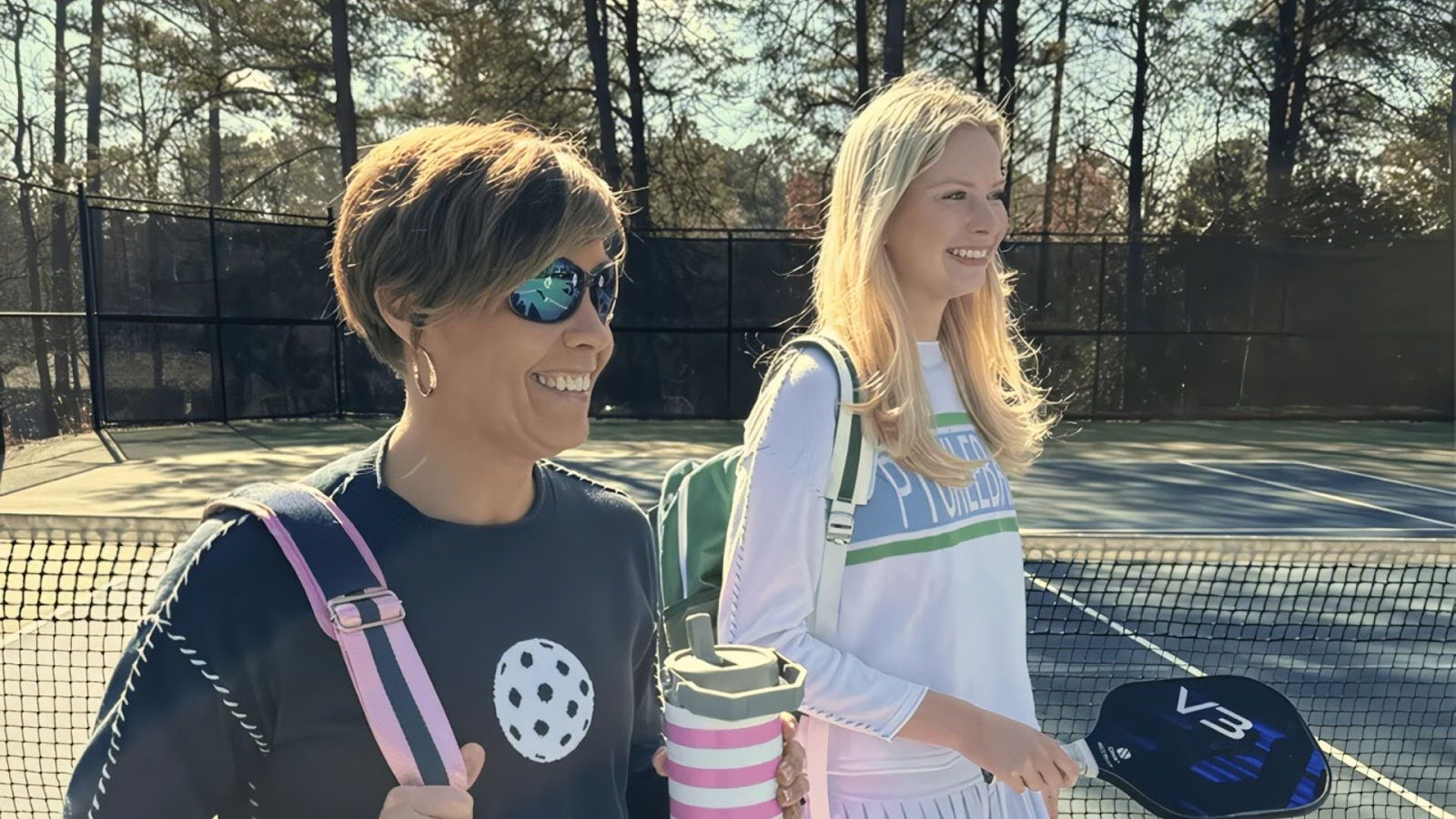 Two women with pickleball gear walking on a sunny outdoor pickleball court