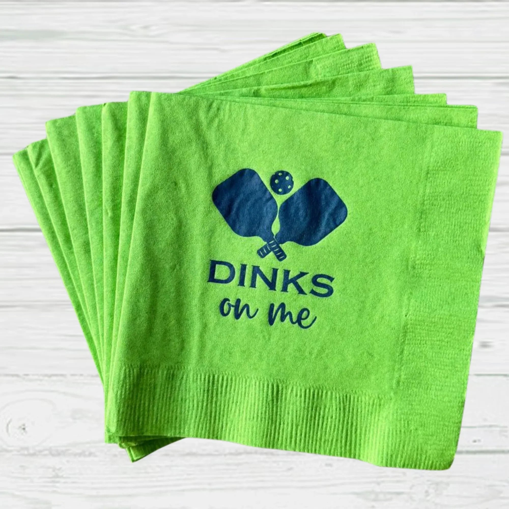 Green pickleball party napkins with blue paddles and ball, text 'DINKS on me'.