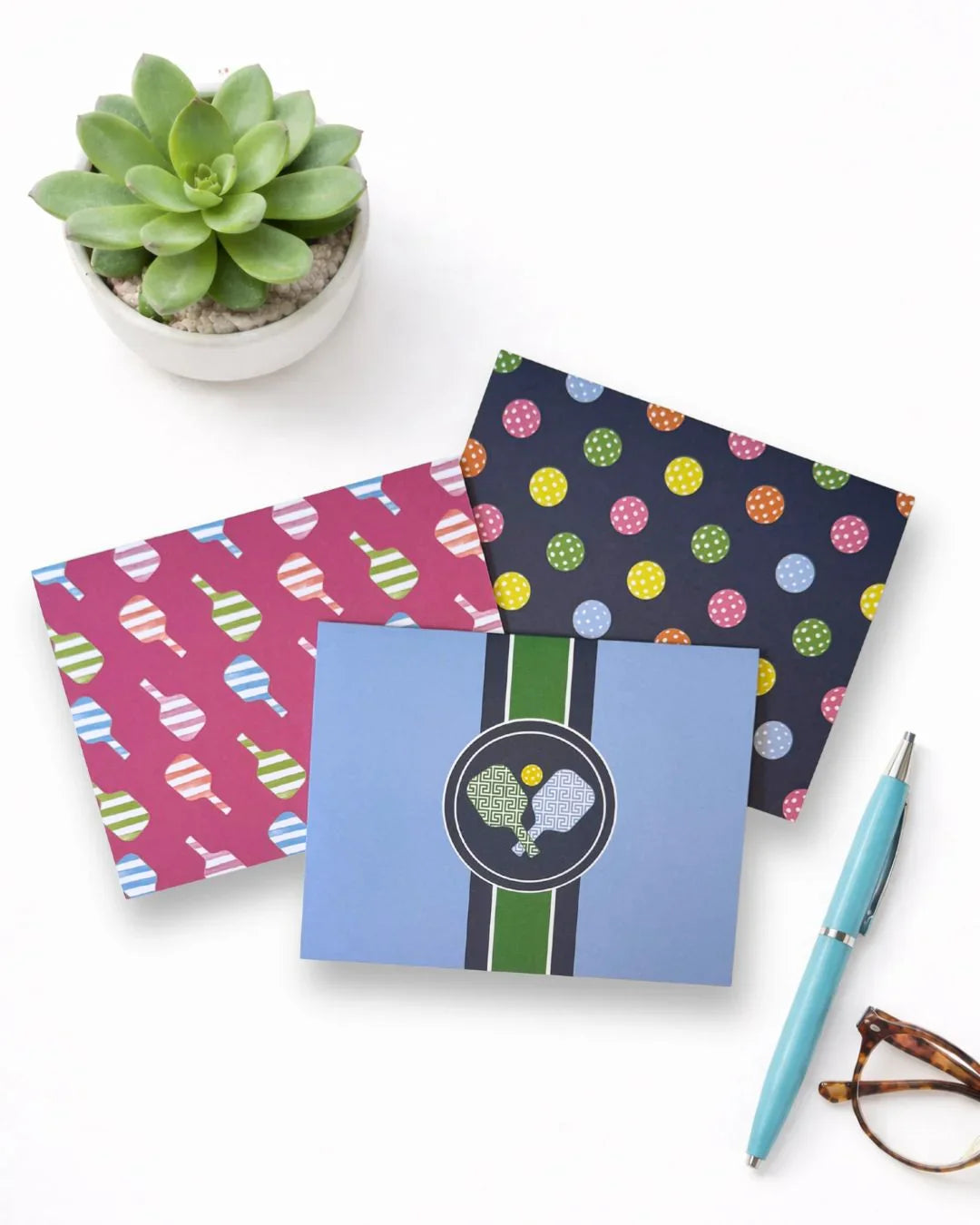 Pickleball-themed notecards with paddle and ball designs, succulent, pen, and glasses on desk
