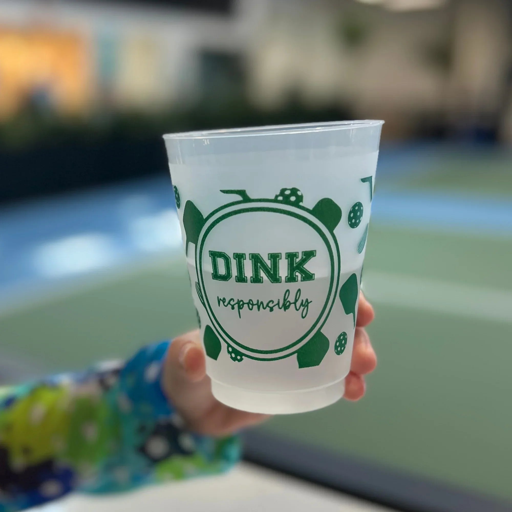 Hand holding a plastic cup with 'Dink responsibly' text on a pickleball court
